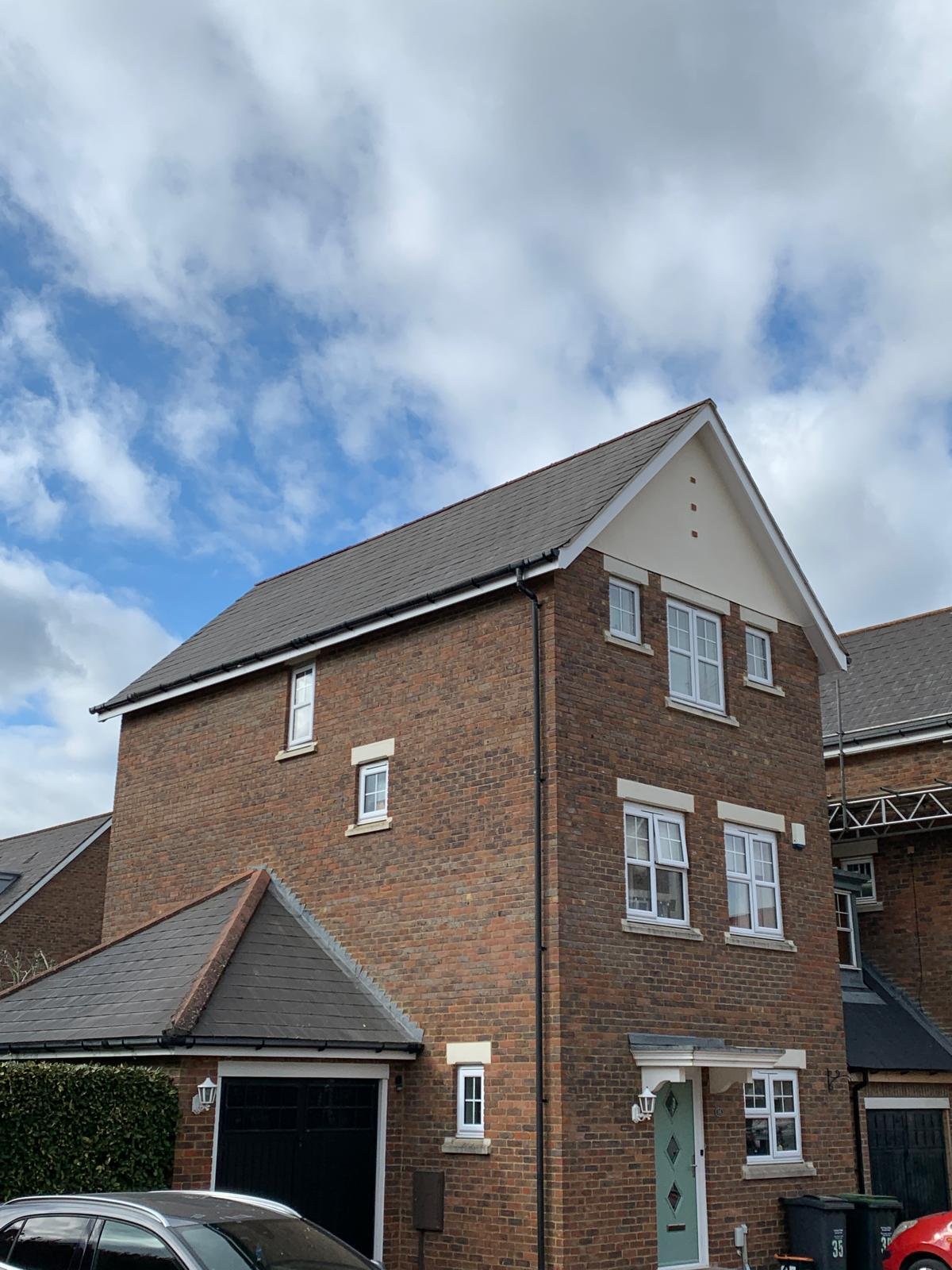Three storey brick house with a grey slate-effect roof and white gable