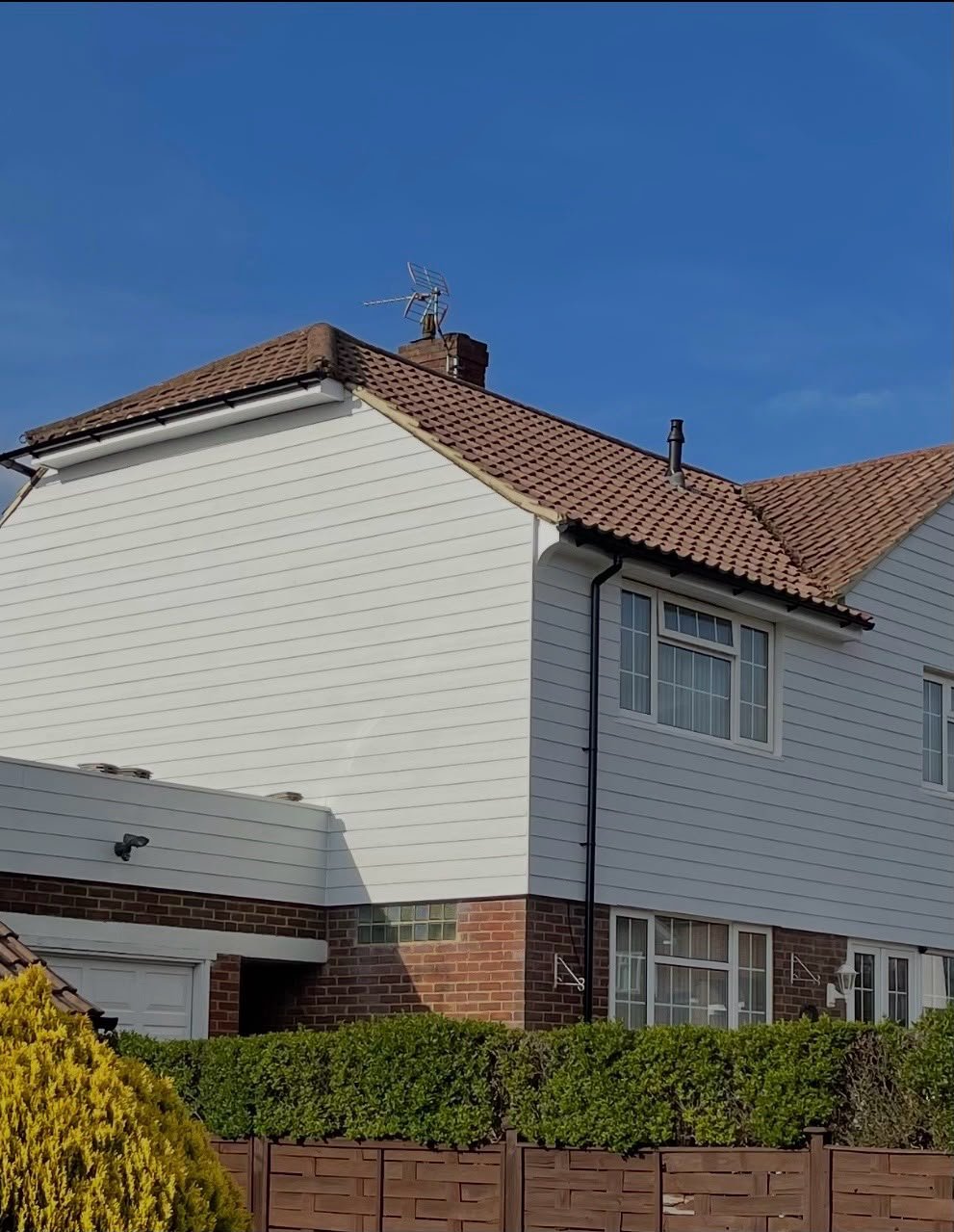 House with white cladding and a red tiled roof under blue sky
