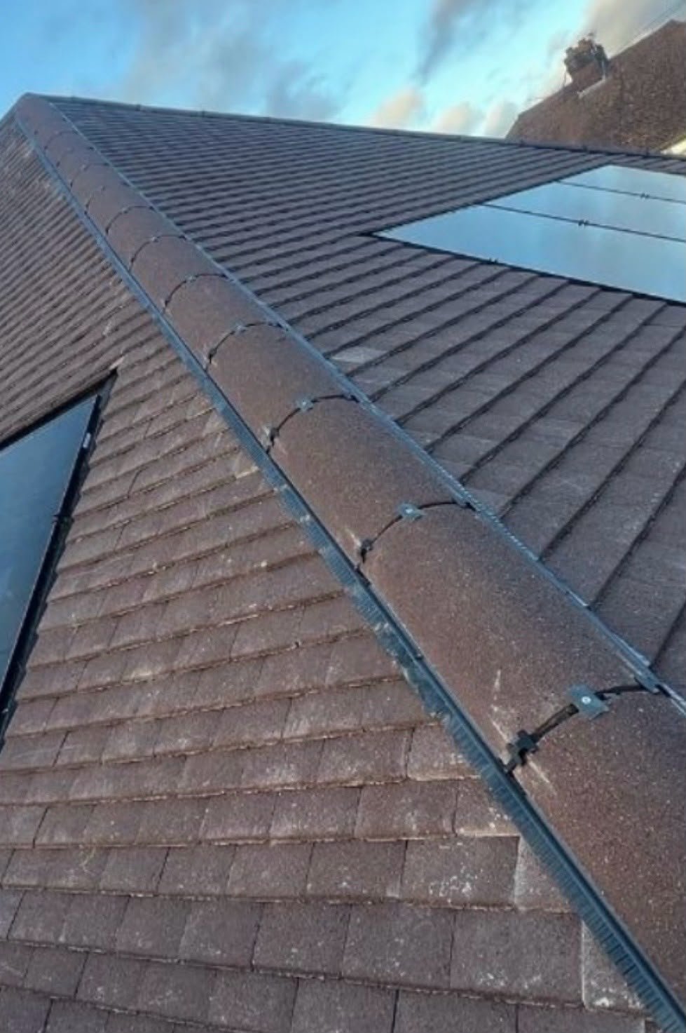 Close-up of a dry ridge system on a brown tiled roof beside solar panels
